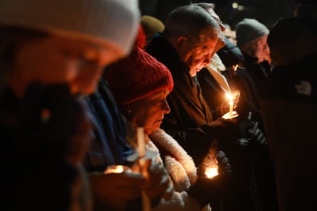 rows of people stand and look down as they hold candles