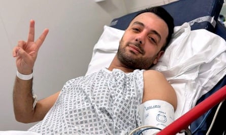 Pouria Zeraati in a hospital bed, gesturing towards the camera