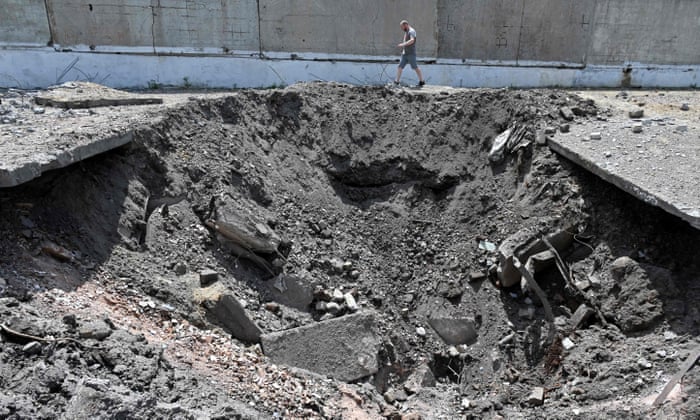 A man walks past a huge crater made from the hit of a Russian rocket in an industrial zone of Kharkiv.