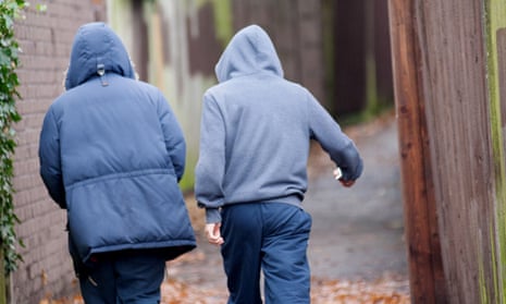 Two teenage boys in hoodies walking together down a suburban alleyway.