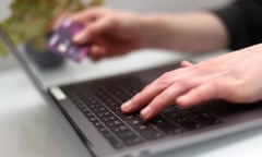 A person using a laptop while holding a bank card.