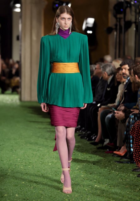 Model walking on catwalk in green and plum coloured outfit