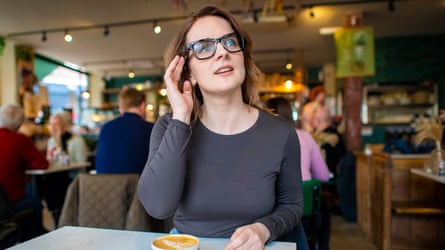 Elle Hunt wearing a pair of Meta Ray-Ban smartglasses while sat at a table in a cafe