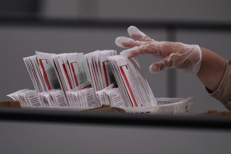 A worker's gloved hand flips through a stack of ballot envelopes.