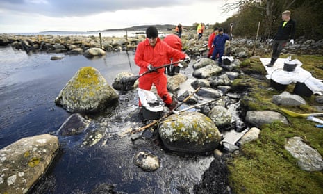 People clean up oil from among the rocks on the shore