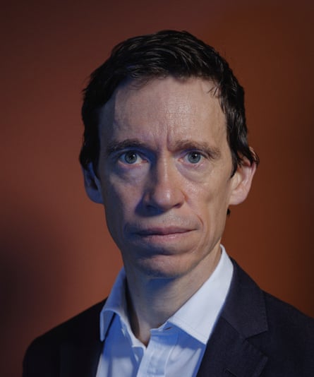 Rory Stewart wearing a navy suit and white shirt against a brown background