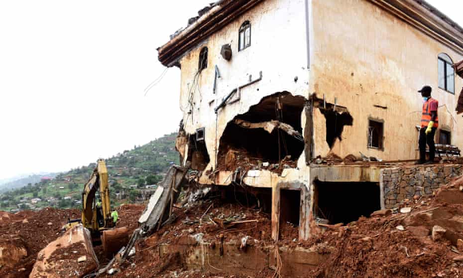 A man looks on as a digger is used to clear mud and debris from a partially collapsed hillside in Freetown