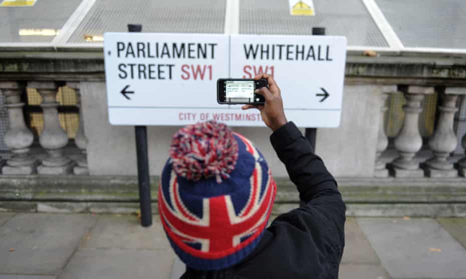 A tourist photographing the Parliament Street/ Whitehall sign, London.