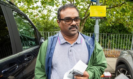 Clement Laurence, standing in car park between two cars, wearing grey polo shirt and green rainproof jacket