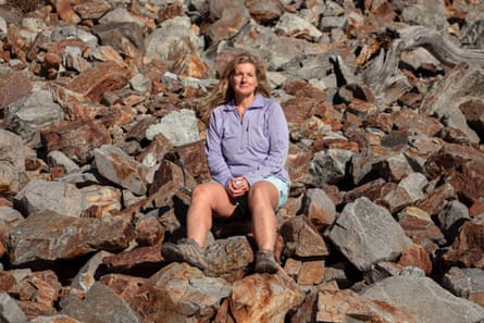 A woman sitting on a rock amid a rockfall, smiling.