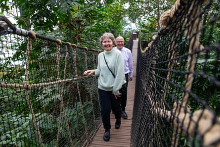 Two people smile as they cross a rope and wood bridge