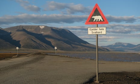 Mountains nearly devoid of snow stand behind a road and a polar bear warning sign during a summer heatwave on Svalbard archipelago in July near Longyearbyen, Norway.