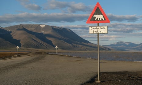 Mountains nearly devoid of snow stand behind a road and a polar bear warning sign during a summer heat wave on Svalbard archipelago in 2020.