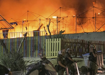 Riot police stand guard as a large fire burns inside the Moria refugee camp last September