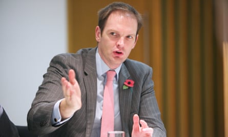 Dan Poulter, in a pale grey suit, gesticulates as he speaks at a roundtable event