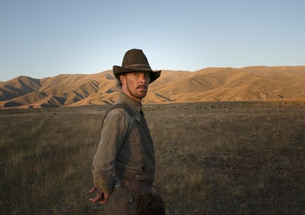 A western cowboy stands in a field with a low sun
