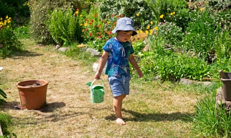 Child wearing a sunhat walking on parched lawn with a watering can