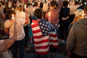 A man has a US flag draped around him and he and others hold up lit candles in the shape of the crucifix