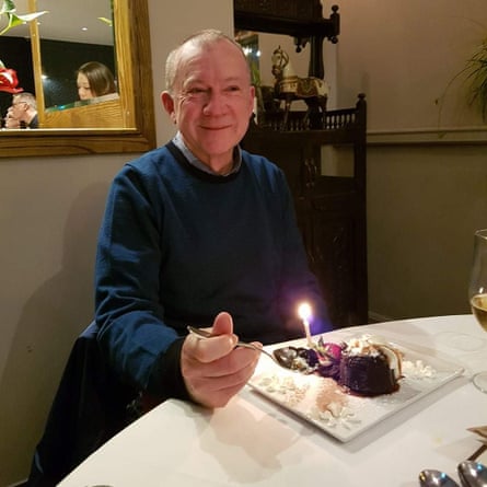 Des, an older man, smiling, sitting before a cake with candle