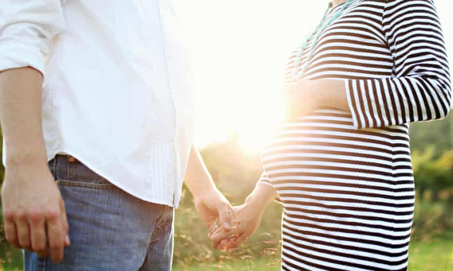Pregnant Caucasian couple holding hands in field