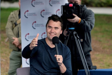 Charlie Kirk holds a microphone and outstretches his hand for a handshake