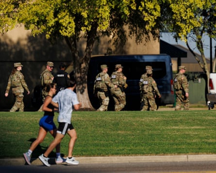 Man and woman jog past group of guards in fatigues.