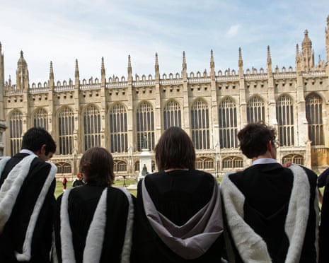 A group of private school students sit in front of an abbey wearing robes
