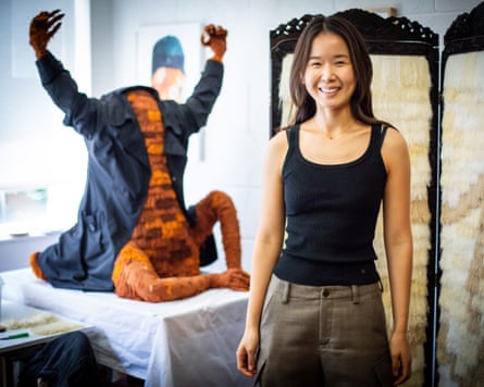 Artist Woo Jin Joo standing with one of her works – an animal like figure in a blue jacket with arms aloft