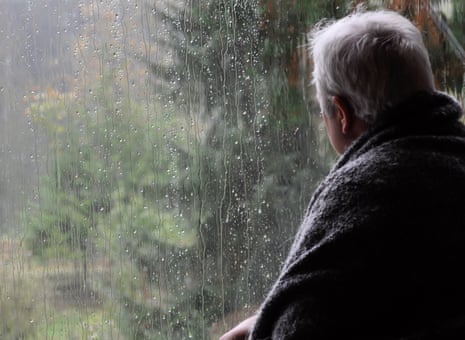 Man wrapped in a blanket looking out of a window on a rainy day