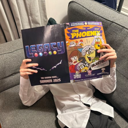 Child reading a copy of The Phoenix (face obscured by comic) while lying on a grey sofa.