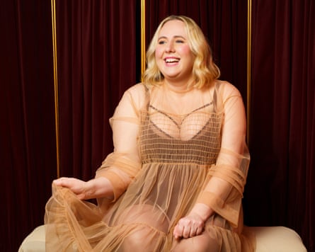 Comedian Helen Bauer sitting down and smiling while wearing a brown dress.