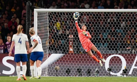 Earps diving high to her right to get one hand on the ball as two England defenders look on