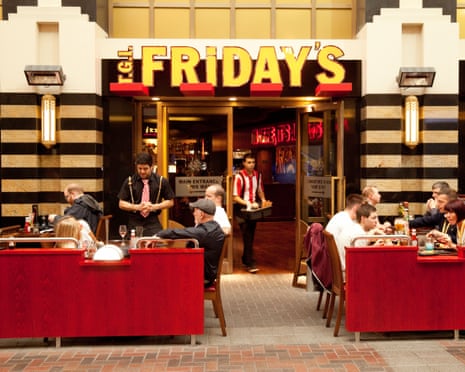 Waiter serving people eating at TGI Fridays restaurant, the O2 arena, London UK.