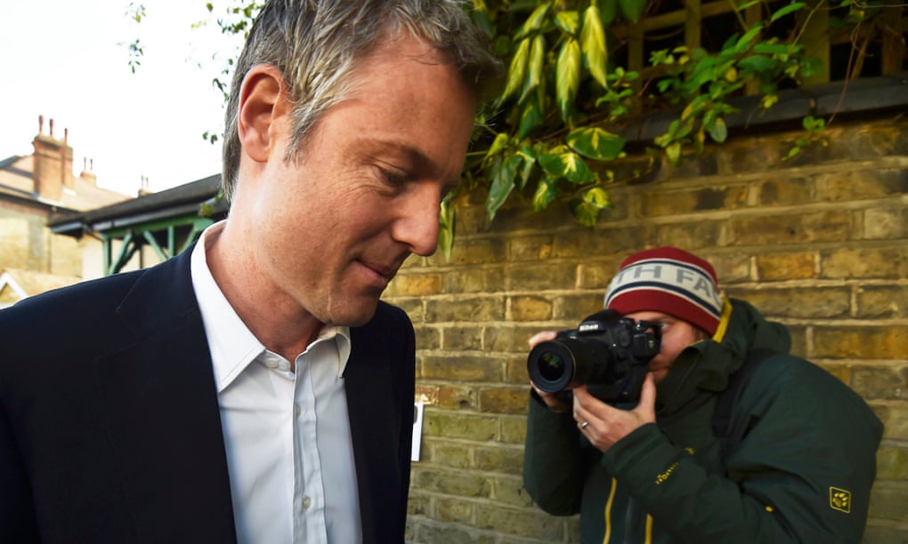 Zac Goldsmith looking sheepish and being snapped by a photographer wearing a beanie hat