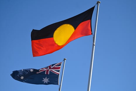 An Aboriginal flag is seen next to the Australian flag against a blue sky