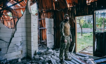 A soldier stands in a dilapidated building looking at the camera
