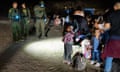 A nighttime image of young children and adults standing in a circle of light from a border patrol officer's flashlight.