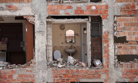 A destroyed house with the wall missing exposing what would have been the bathroom, with the toilet still intact toilet is shown