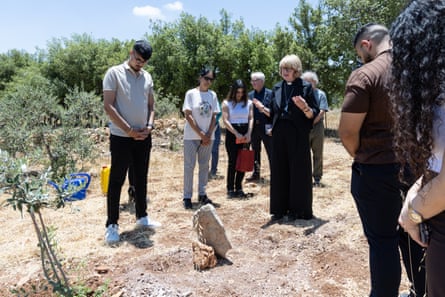 Sarah Mullally standing next to a tree with her hands raised in prayer, surrounded by people with their heads bowed