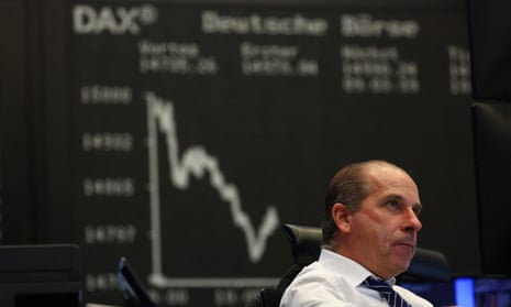 A trader sitting at his desk while behind him a large screen shows the recent fall in the Dax index