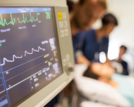 Heart rate monitor, patient and doctors in background in intensive care unit.