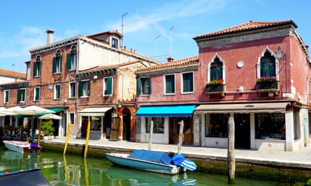 Boat on a canal outside a parade of shops in Murano, Veneto, Italy.