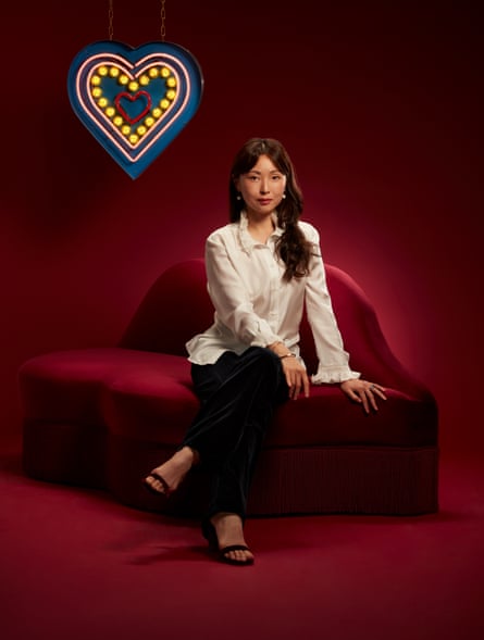 Juhea Kim photographed on a red sofa with an illuminated heart behind her