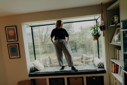 Hannah stands at a picture window wearing adjustable waistband trousers.