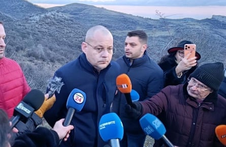 Zahari Vaskov surrounded by journalists holding their microphones out to him against a backdrop of the mountains