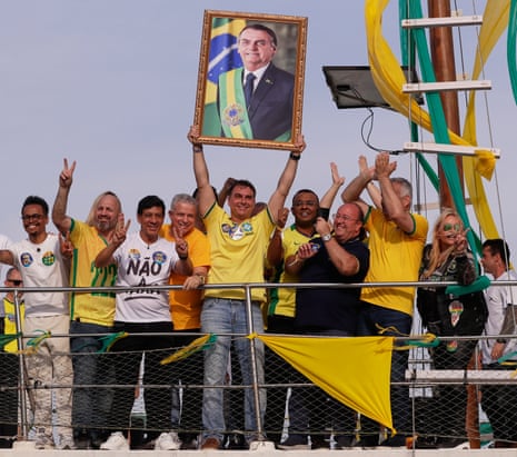 Flavio Bolsonaro holds a portrait of his father while a cheering group poses on a boat