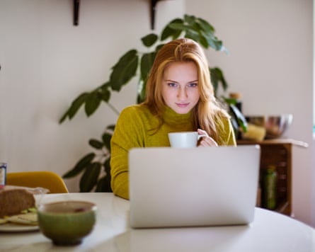 Young woman sitting at table looking at her laptop and drinking coffee