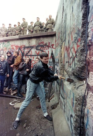 A demonstrator pounds away the Berlin Wall as East Berlin border guards look on from above the Brandenburg Gate on 11 November, 1989
