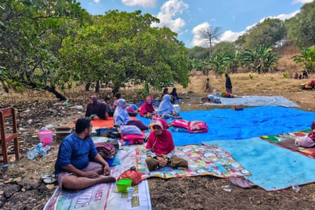 People sit on mats after spending the night in an open field
