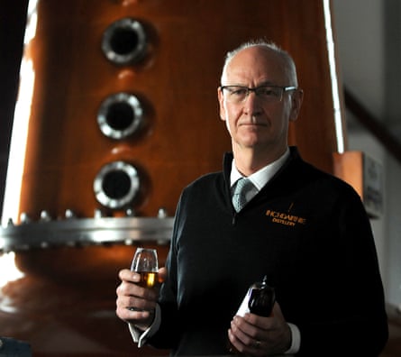 Ian Palmer devant un alambic en cuivre brillant, tenant un verre de whisky